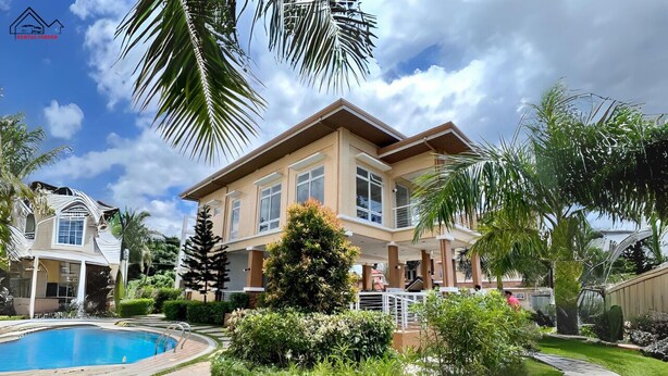 Una amplia casa de dos pisos con piscina, rodeada de exuberante follaje y palmeras.
