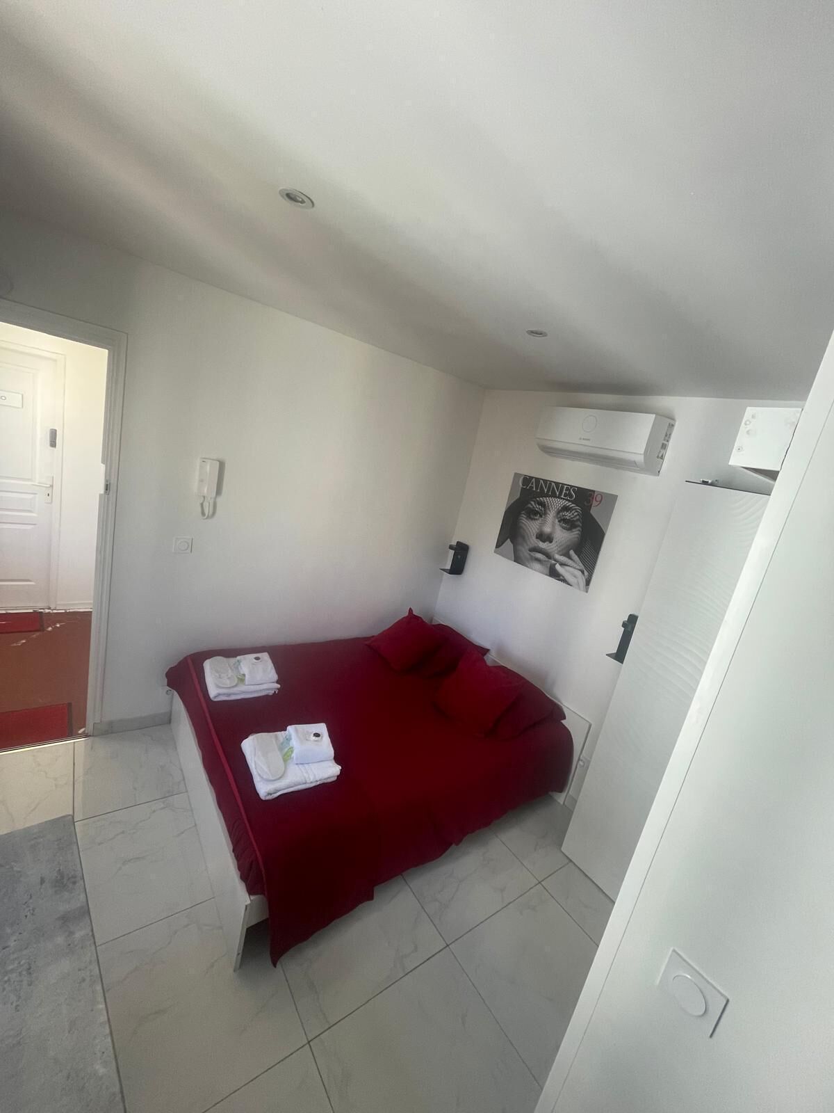 A small, clean room with a bed, a white wall, and a door.