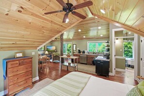 Ein geräumiges Schlafzimmer im Loft-Stil mit einem großen Bett, Holzbalkendecke und Deckenventilator.