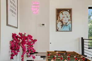 A room with a foosball table, a neon sign, a framed picture, and a wall with a motivational quote. - Luxury Dolly-Themed Cabin, Indoor Pool, Hot Tub (Sevierville)