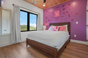 A bedroom with a large window, a bed with white bedding, and a purple wall with decorative stickers. - Luxury Dolly-Themed Cabin, Indoor Pool, Hot Tub (Sevierville)