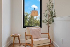 Una habitación con ventana, una silla, una mesita y una lámpara.