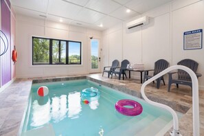 A swimming pool with clear water, surrounded by chairs and a table, and a 'Pool Rules' sign on the wall. - Luxury Dolly-Themed Cabin, Indoor Pool, Hot Tub (Sevierville)