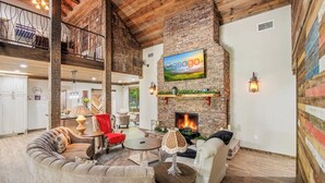 A spacious living area with a fireplace, comfortable seating, and a high ceiling with exposed beams. - Luxe Riverfront Cabin ・ Walk to Parkway・Hot Tub (Pigeon Forge)