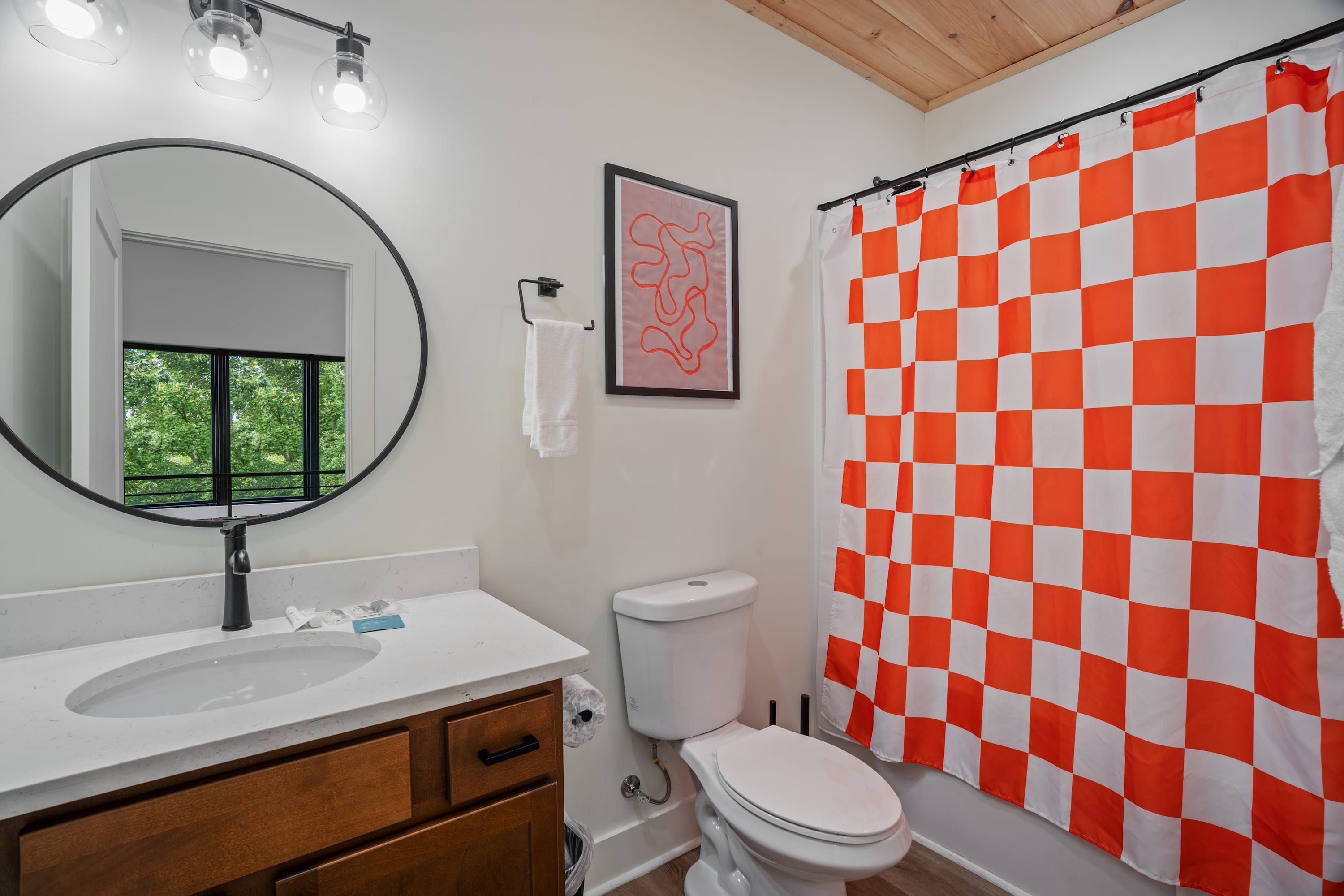 Un baño con lavamanos blanco, inodoro y cortina de ducha a cuadros.