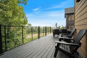 A wooden deck with outdoor furniture, a metal railing, and a view of trees and a distant landscape. - Vols-Themed Luxury Cabin | Indoor Pool | Sleeps 12 (Sevierville)