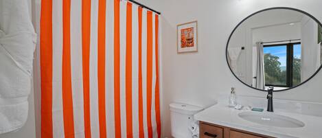 A bathroom with a striped shower curtain, a toilet, a sink with a mirror, and a framed picture on the wall.