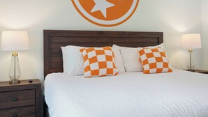 A neatly made bed with white and orange checkered pillows, flanked by two bedside lamps on wooden nightstands.