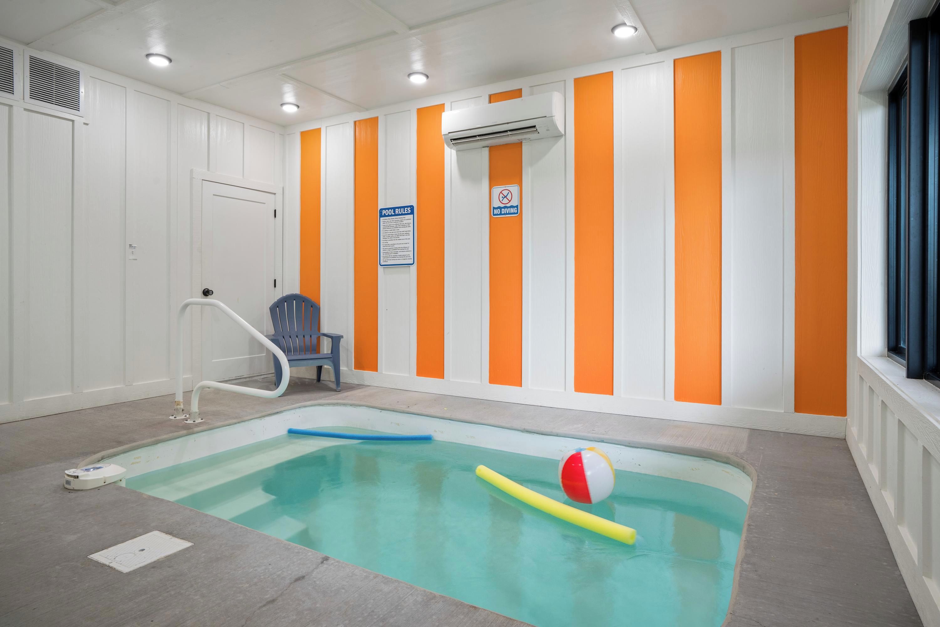 Una piscina interior con un juguete flotante azul y amarillo, una silla azul y un cartel con las normas de la piscina.