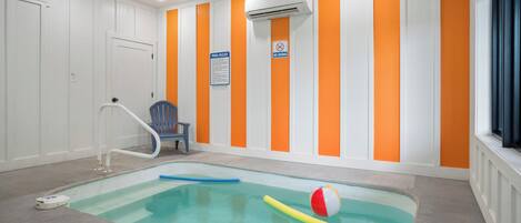 Una piscina interior con un juguete flotante azul y amarillo, una silla azul y un cartel con las normas de la piscina.