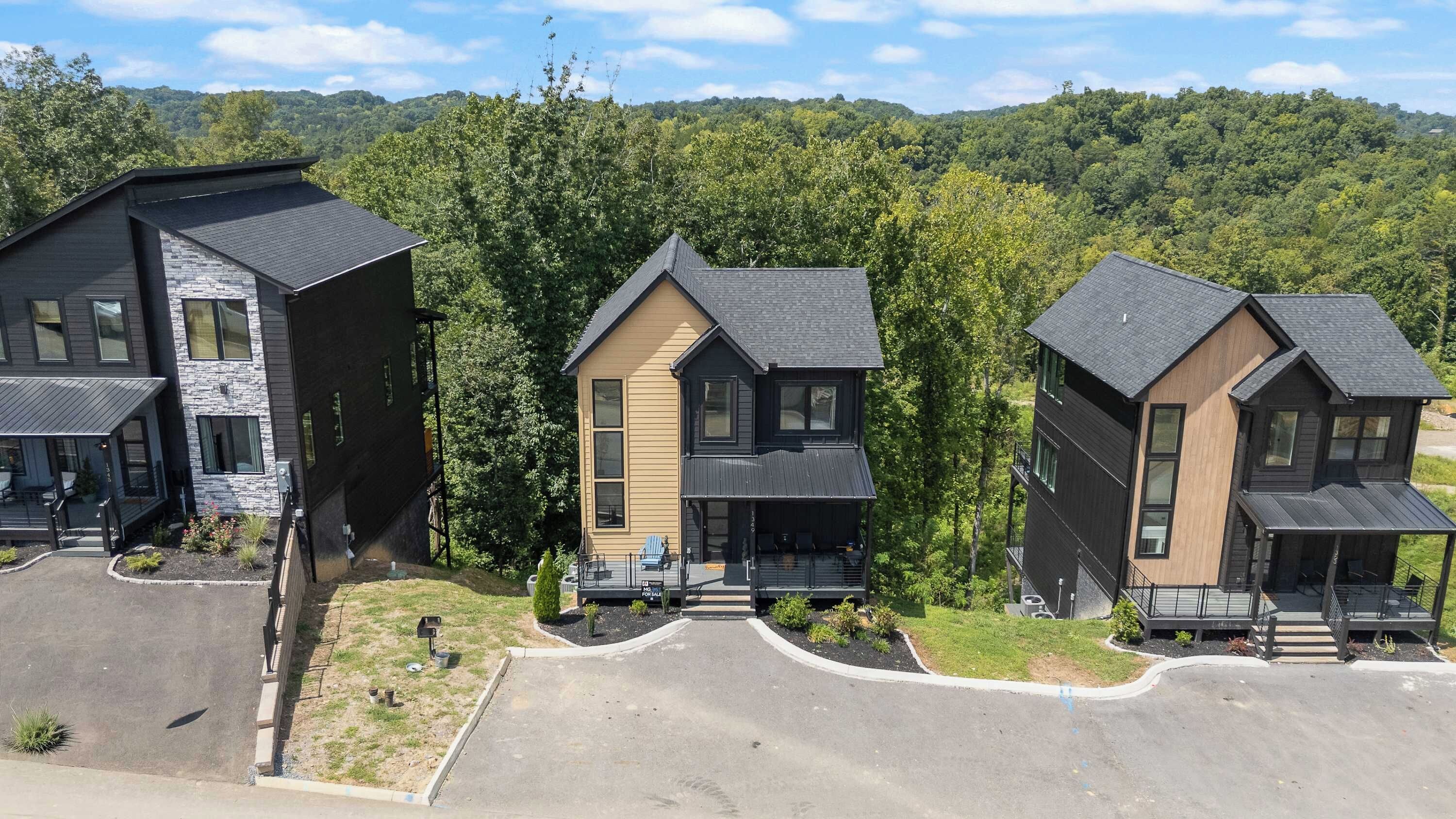 A row of modern multi-story houses with a landscaped driveway and a forested backdrop.