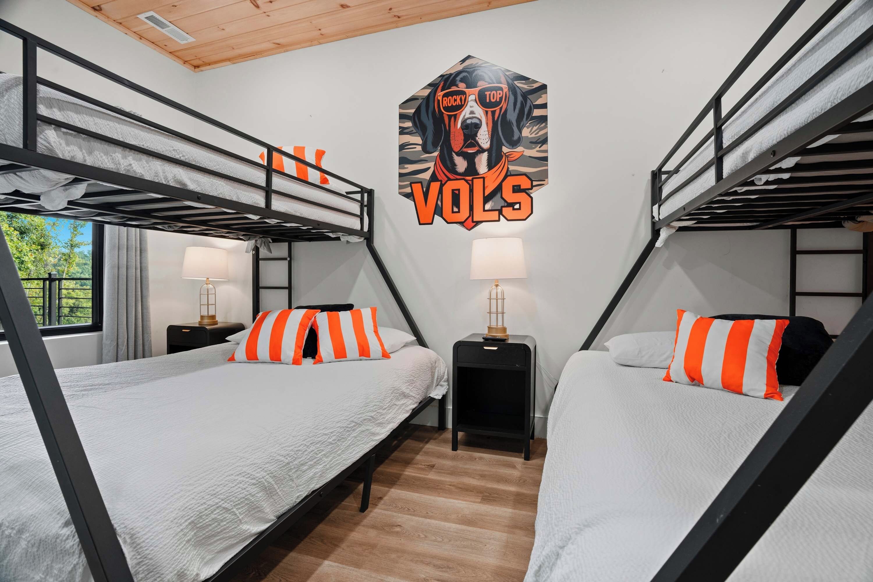 Une chambre avec un lit superposé, dotée de deux lits, chacun agrémenté d’un oreiller à rayures orange et blanches, d’une lampe fixée au mur et d’une grande affiche représentant un chien portant des lunettes de soleil.