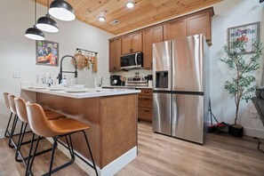 A modern kitchen with a central island, stainless steel appliances, wooden cabinets, and a bar stool seating area. - Vols-Themed Luxury Cabin | Indoor Pool | Sleeps 12 (Sevierville)