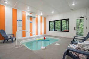 A small indoor pool with a blue pool ladder, two lounge chairs, a window with a view of trees, and a sign indicating no diving. - Vols-Themed Luxury Cabin | Indoor Pool | Sleeps 12 (Sevierville)