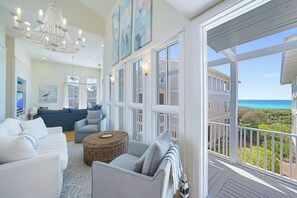 A spacious living room with a large window, a chandelier, and a view of the ocean. - Renovated Beachside Seaside Home; Porches, Outdoor Dining & Serene Gulf Views (Santa Rosa Beach)