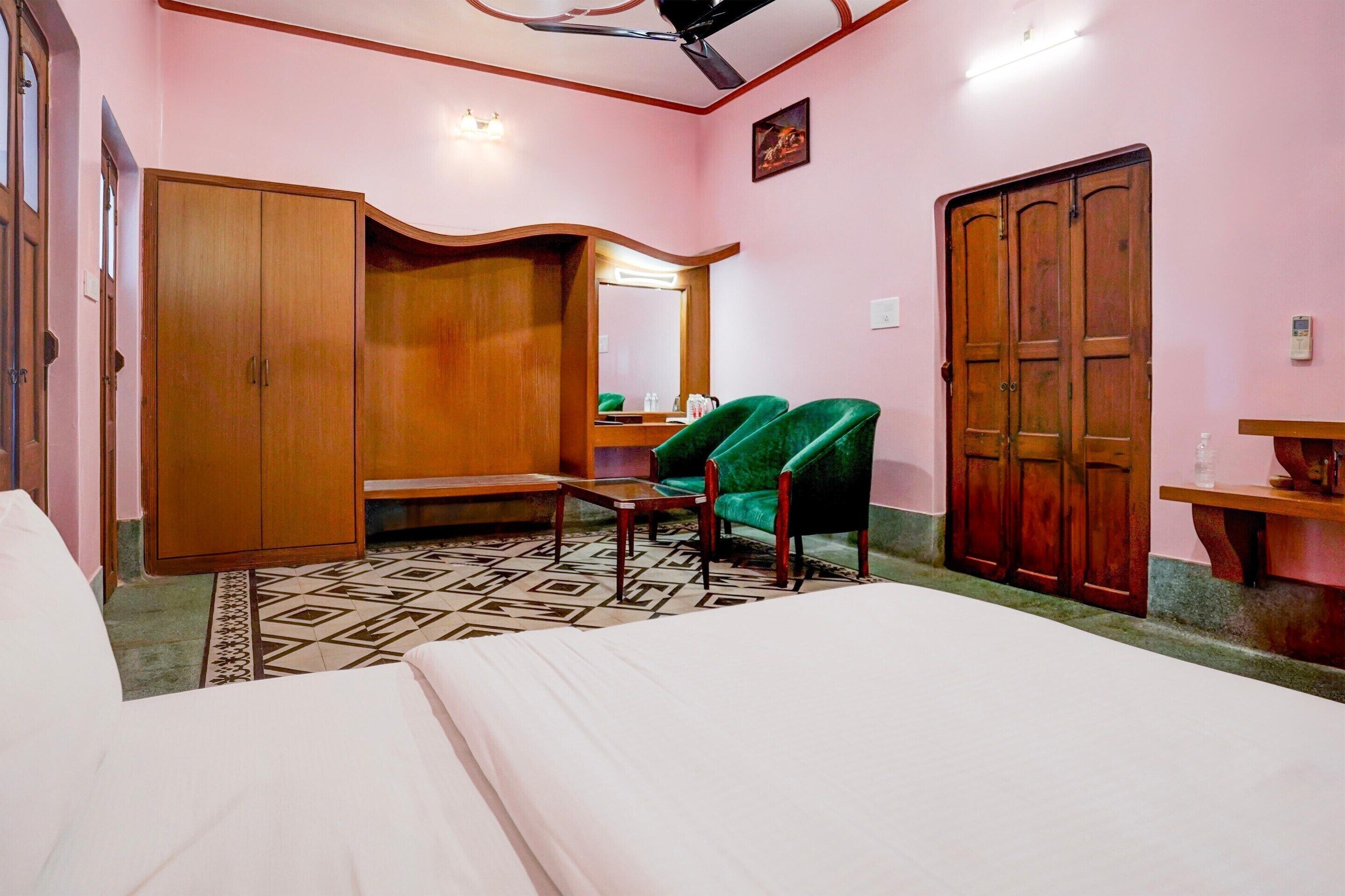 Un dormitorio con una cama, una silla verde, un armario de madera y un espejo.