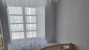 A bedroom with a wooden bed, a chair, a window with lace curtains, and a chandelier. - Casa Grande (Coín)