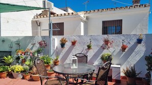 A patio with a round table and chairs, surrounded by potted plants and a white wall with windows. - Casa Grande (Coín)