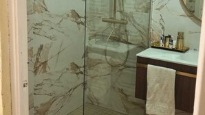 A bathroom with a glass-enclosed shower, marble walls, a wooden floor, a white sink, and a mirror. - Casa Grande (Coín)