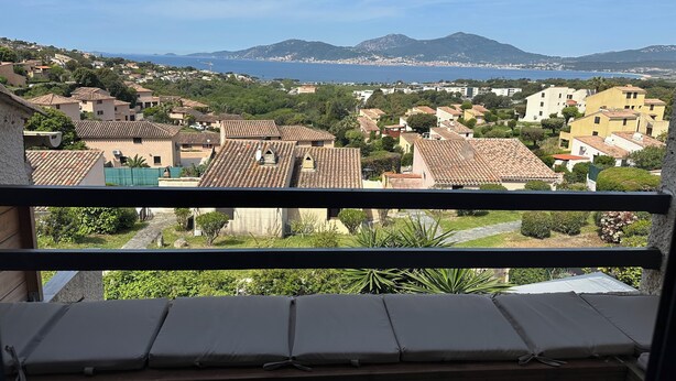 Ein Balkon mit Blick auf eine Küstenstadt, Häuser mit Terrakotta-Dächern und eine entfernte Bergkette.