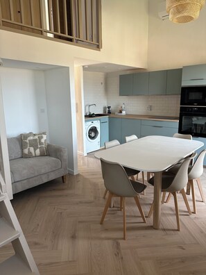 A modern kitchen with light blue cabinets, a built-in washing machine, and a dining area with a white table and chairs. - 3-bedroom apartment with panoramic sea view (Grosseto-Prugna)