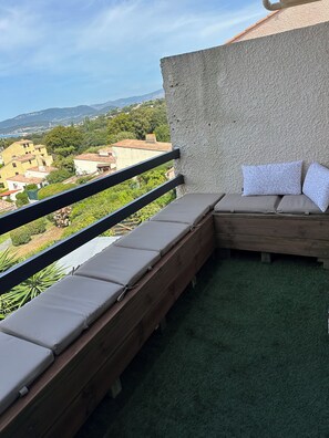 A balcony with a view of a cityscape, a wooden bench with cushions, and a textured wall. - 3-bedroom apartment with panoramic sea view (Grosseto-Prugna)