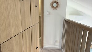 Eine Holztreppe führt zu einer Zwischenebene mit einer Wandleuchte und einem an der Decke befestigten Gerät.