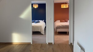 A room with two beds, wooden flooring, and a white door leading to another room. - Magnificent renovated farmhouse in peaceful countryside setting (Rives-du-Couesnon)