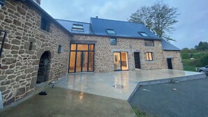 A stone building with a large glass door, a covered patio, and a car parked outside. - Magnificent renovated farmhouse in peaceful countryside setting (Rives-du-Couesnon)