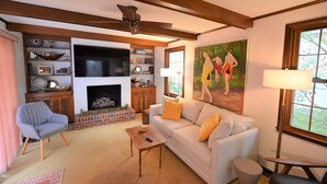A living room with a fireplace, a sofa, a chair, a coffee table, and a painting on the wall. - Quaint Pet Friendly Home In South Rehoboth! (Rehoboth Beach)