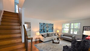 A staircase leading to a living area with a white sofa, a patterned armchair, and a painting on the wall. - Quaint Pet Friendly Home In South Rehoboth! (Rehoboth Beach)