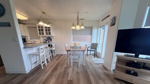Una cocina moderna con armarios blancos, un comedor con mesa y sillas de madera, y un televisor sobre un mueble de madera.