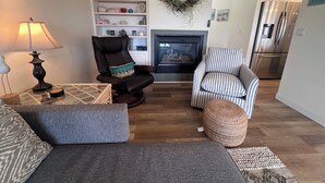 Una sala de estar con chimenea, un sillón a rayas, un sillón de cuero, un sofá y una lámpara.