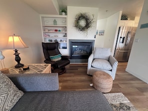 Een woonkamer met een open haard, een gestreept fauteuil, een leren stoel, een bank en een lamp.