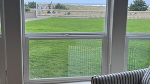 Una habitación con un ventanal grande que da a una zona verde y una vista lejana del mar.