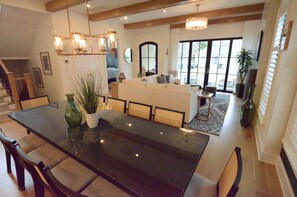 A spacious living area with a large dining table, comfortable seating, a chandelier, and a view through large windows. - Beautiful Brand New Single Family Home With Private Pool! (Rehoboth Beach)