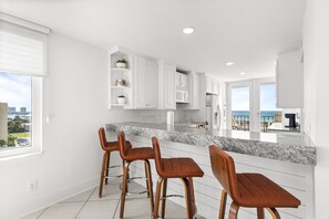 A modern kitchen with white cabinetry, a granite countertop, and three wooden bar stools. - 🏖️ Santa Rosa Dunes 1061: Steps to the Gulf, Pool + Stunning Sound Views! (Pensacola Beach)