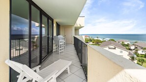 En balkon med hvide stole, et bord og havudsigt.