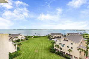 A residential area with houses, a grassy lawn, and a body of water in the background. - 🏖️ Santa Rosa Dunes 1061: Steps to the Gulf, Pool + Stunning Sound Views! (Pensacola Beach)