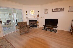 A living room with a fireplace, a television, and a floral armchair. - Townhouse Close to Route One and Downtown Rehoboth Beach! (Rehoboth Beach)
