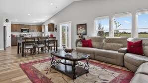 A spacious living area with a glass coffee table, a beige sofa, and a dining area with wooden furniture. - Sweet Esmeralda-FirePit, BBQ, Pets OK, Fenced Yard (Nampa)