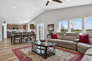 A spacious living area with a glass coffee table, a beige sofa, and a dining area with wooden furniture. - Sweet Esmeralda-FirePit, BBQ, Pets OK, Fenced Yard (Nampa)