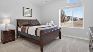 A bedroom with a bed, a nightstand, a lamp, a framed picture, and a large window with a view of a residential area. - Sweet Esmeralda-FirePit, BBQ, Pets OK, Fenced Yard (Nampa)