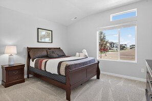 A bedroom with a bed, a nightstand, a lamp, a framed picture, and a large window with a view of a residential area. - Sweet Esmeralda-FirePit, BBQ, Pets OK, Fenced Yard (Nampa)