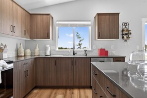 A modern kitchen with wooden cabinets, a stainless steel countertop, and a window providing a view of the outdoors. - Sweet Esmeralda-FirePit, BBQ, Pets OK, Fenced Yard (Nampa)