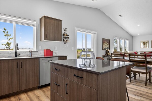 A modern kitchen with a large island, wooden cabinets, and a view of the outdoors.