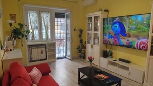 Una sala de estar con un sofá rojo, una mesa de centro, un televisor y un puerta corrediza de vidrio que da a un balcón.