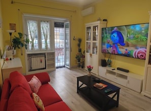 Ein Wohnzimmer mit einem roten Sofa, einem Couchtisch, einem Fernseher und einer Glasschiebetür, die auf einen Balkon führt.