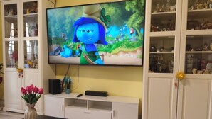 Un salón con una televisión de pantalla plana, una mesa de centro con una revista y un florero con flores.