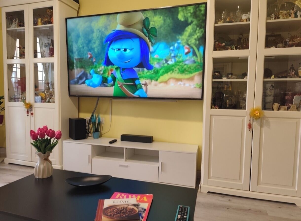 Ein Wohnzimmer mit einem Flachbildfernseher, einem Couchtisch mit einer Zeitschrift und einer Blumenvase.